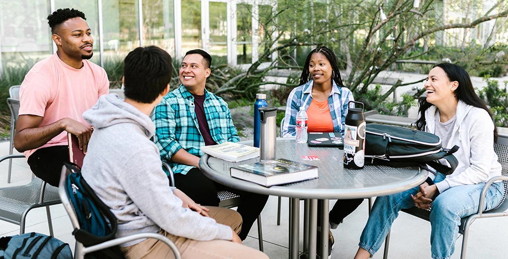 smiling college students sitting at a table to study financial literacy