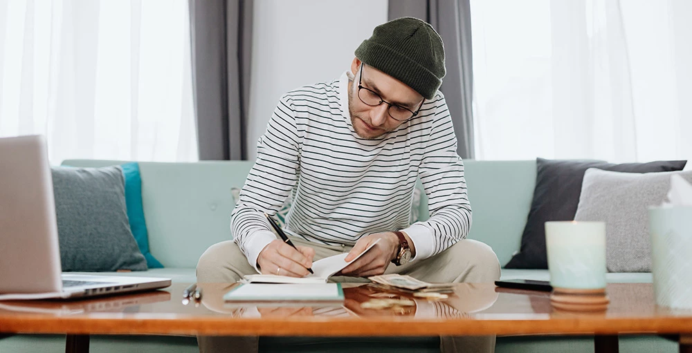 man sitting on couch while reviewing budget and finances in notebook
