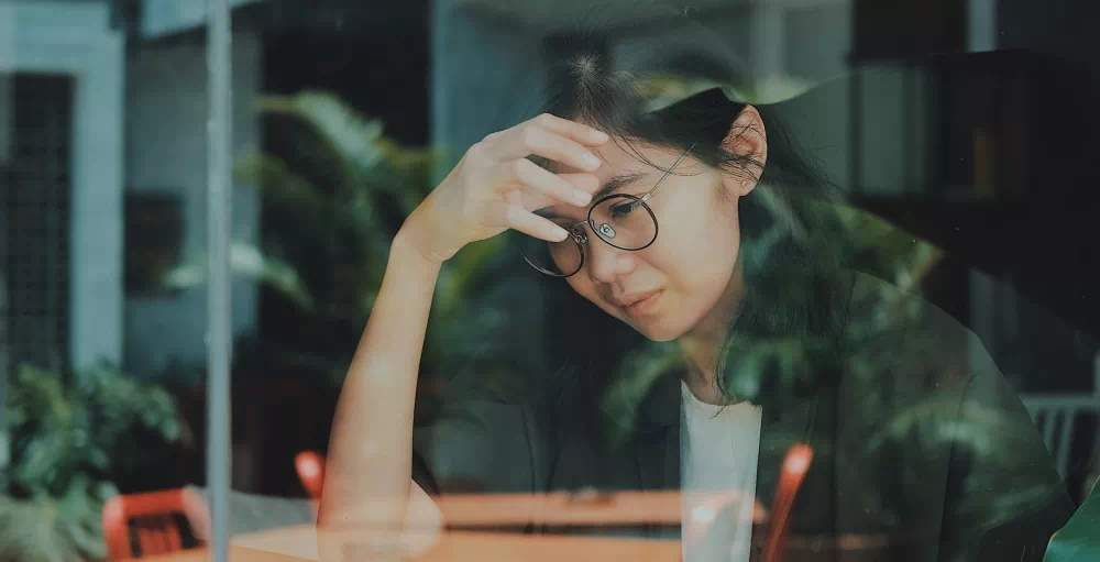 Woman in a coffee shop stressed about her finances looking out a window