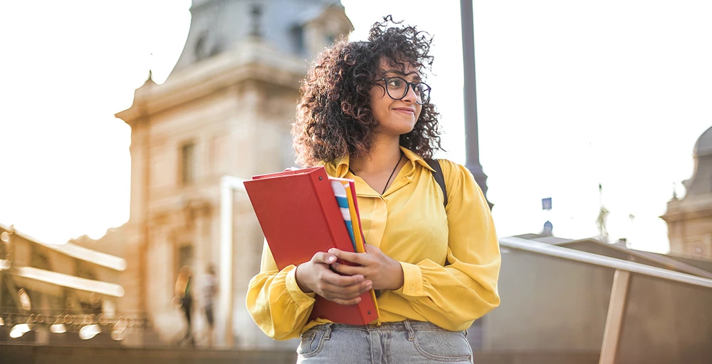 college student in yellow jacket holding textbooks