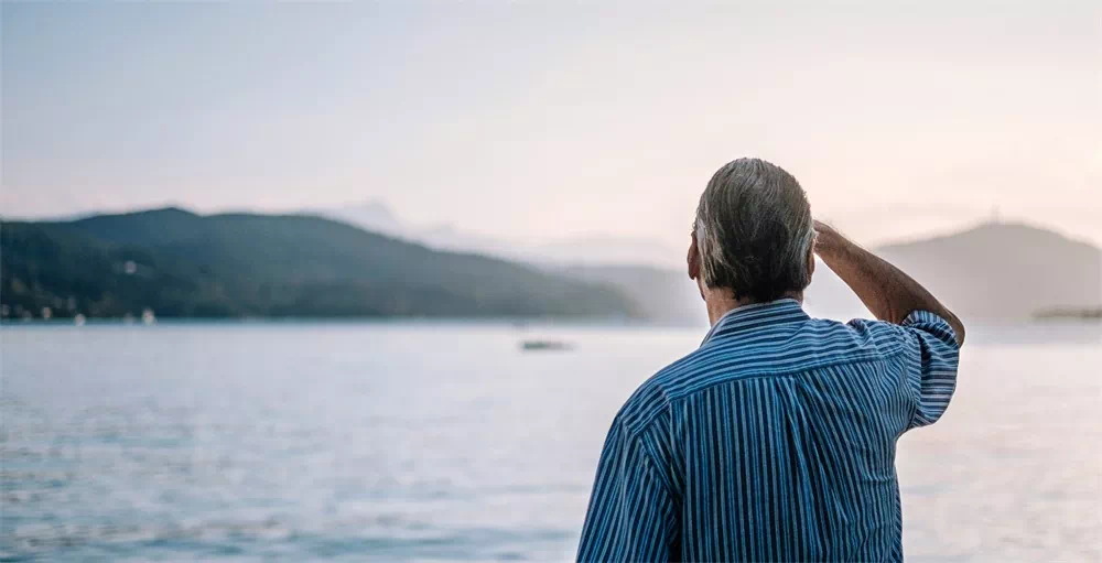 retired man in striped shirt looking out at a lake