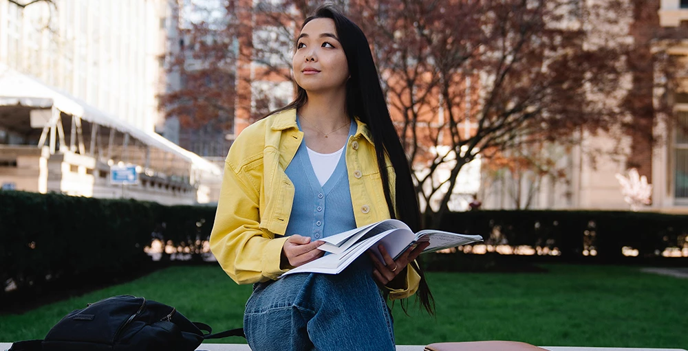 college girl sitting on a bench with her financial wellness notes