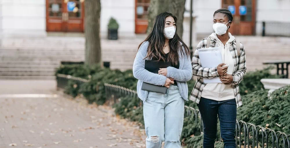 Two women students with masks walking through a college campus