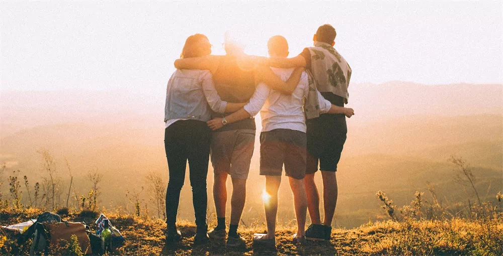 four college students with hands wrapped around shoulders while looking at sunset