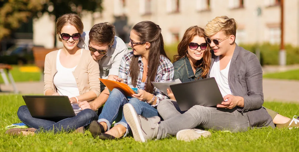 A group of college students sitting on the grass and signing up for the iGrad platform on their computers