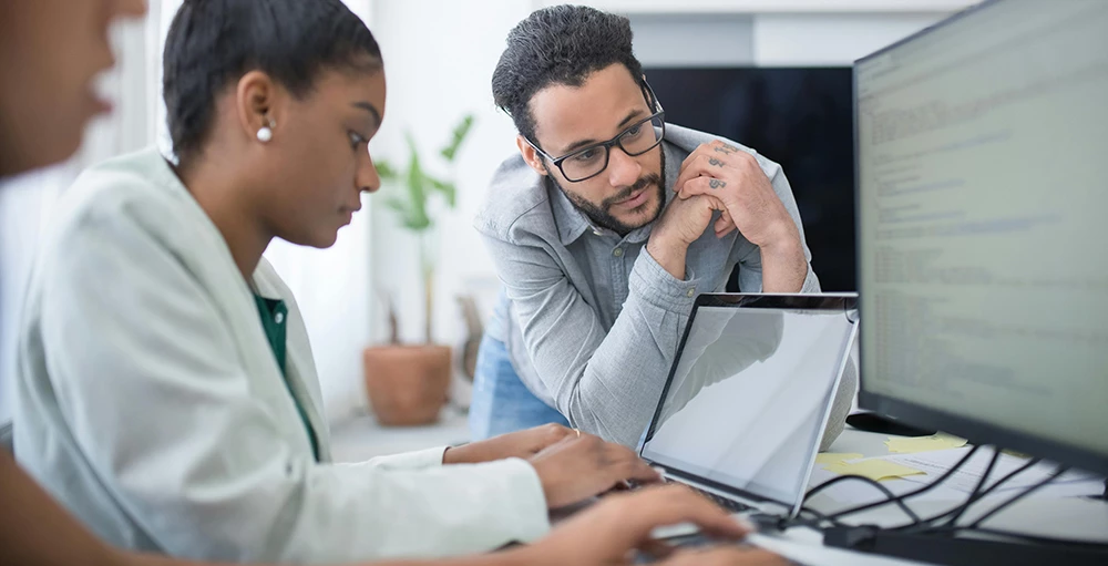 man in gray shirt looking at student's computer