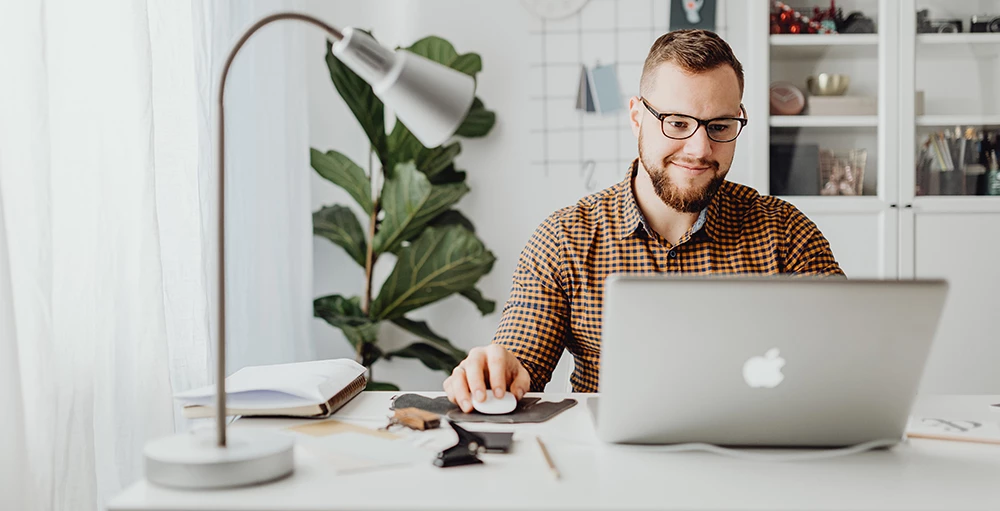 man smiling at his laptop while working on his financial wellness