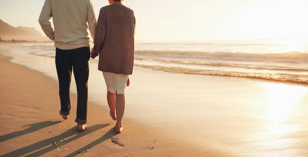 A retired couple walking on the beach holding hands while their passive retirement income grows