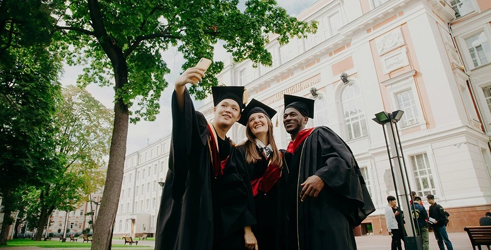 college students in graduation gowns taking a photo together on campus
