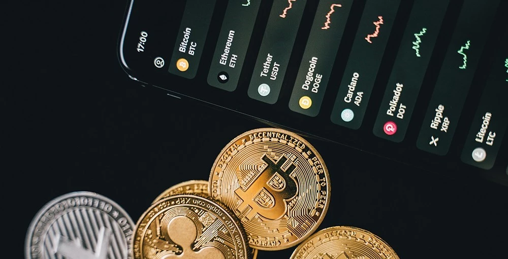 bitcoins beside a phone displaying crypto rates