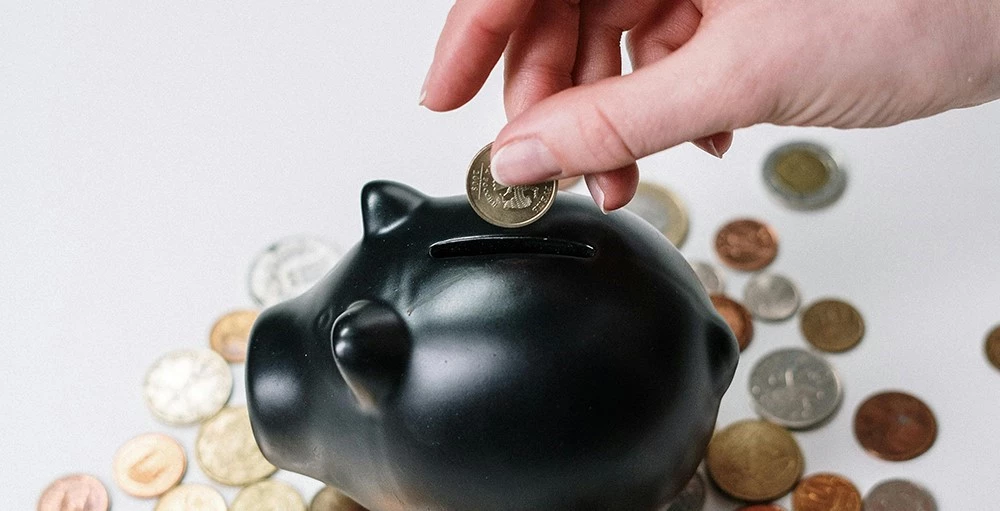 person putting coins in a piggy bank