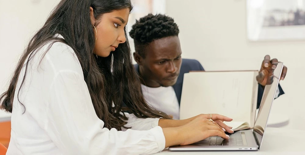 woman using a laptop beside a man reading a book