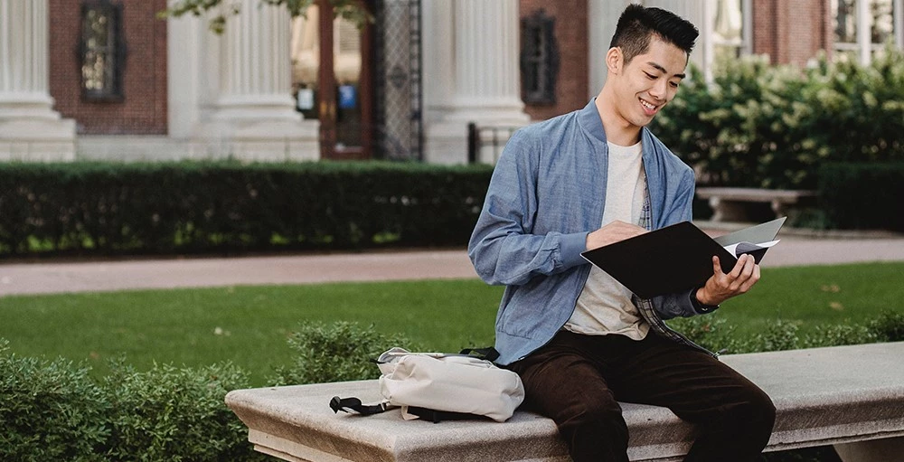 college student sitting on bench and reading documents