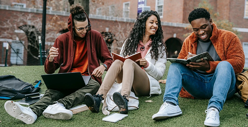 college students with books sitting near university